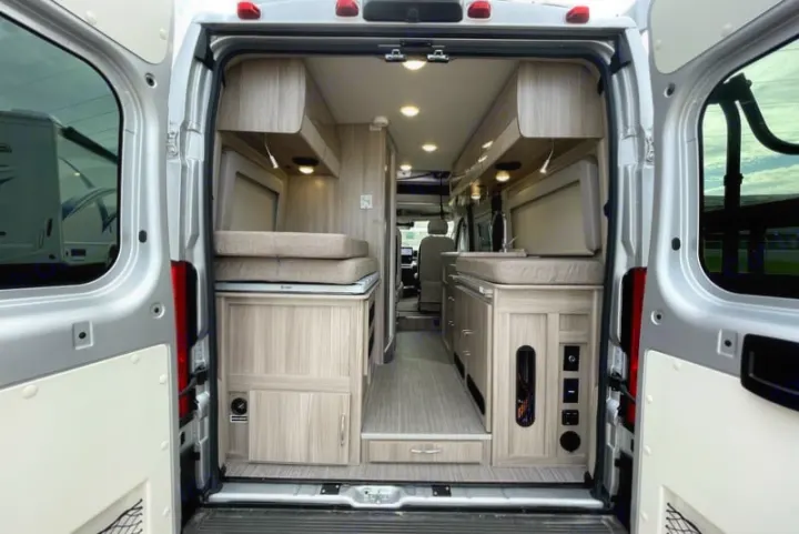 Open rear view of a modern RV rental camper van's interior, featuring light wood cabinets, bed, and kitchen area.. Thor Scope 2023