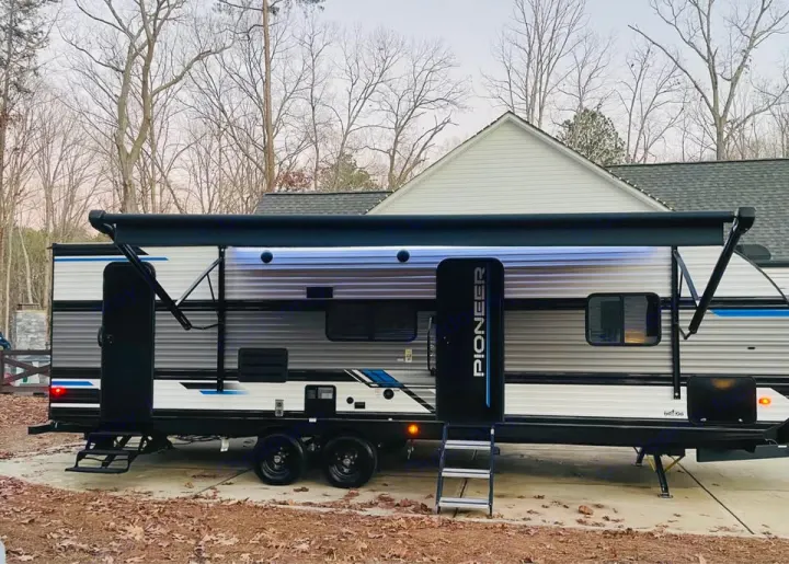 A modern Pioneer travel trailer (RV) with an extended awning and blue lights, parked. Perfect for your next RV rental adventure.. Heartland RVs Pioneer 2023