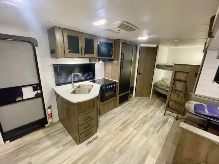 RV rental interior: a modern kitchen, bunk beds, and dining area on light wood-look flooring.. Heartland RVs Pioneer 2023