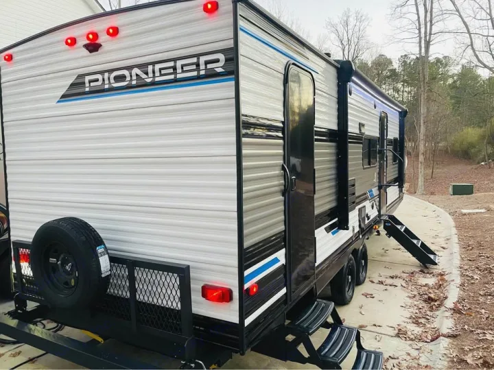 New "Pioneer" travel trailer, perfect for an rv rental. Gray & black exterior with extended awning, rear spare, and steps.. Heartland RVs Pioneer 2023
