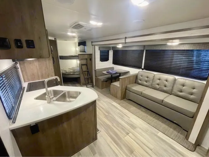 Explore this RV rental's spacious interior, featuring a cozy sofa, dining area, kitchen with a sink, and rear bunk beds.. Heartland RVs Pioneer 2023