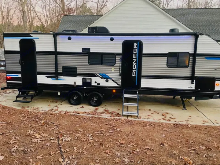 Stylish gray & white travel trailer RV rental with blue accents, extended awning & steps. Parked on a driveway.. Heartland RVs Pioneer 2023