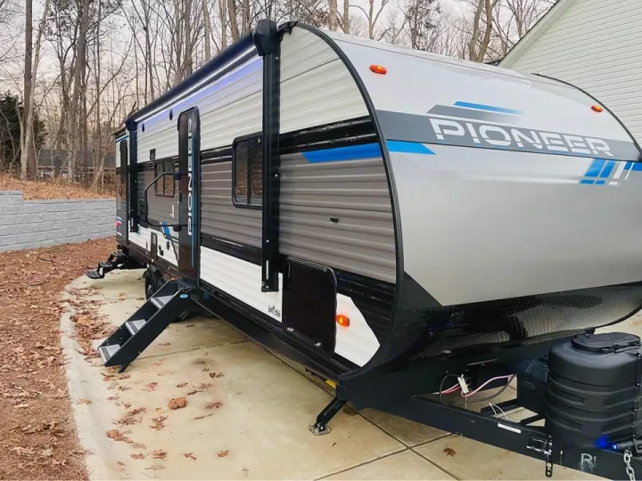 This modern Pioneer travel trailer, perfect for rv rental, is parked outdoors. It features an extendable awning with lights and deployable steps.. Heartland RVs Pioneer 2023