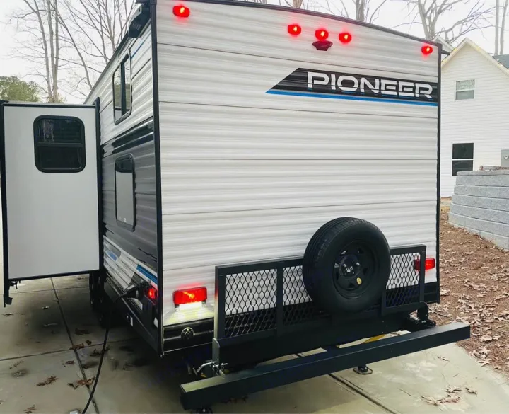 Rear of a white Pioneer travel trailer, ideal for your next RV rental. Shows a spare tire, cargo rack, and red LED lights.. Heartland RVs Pioneer 2023