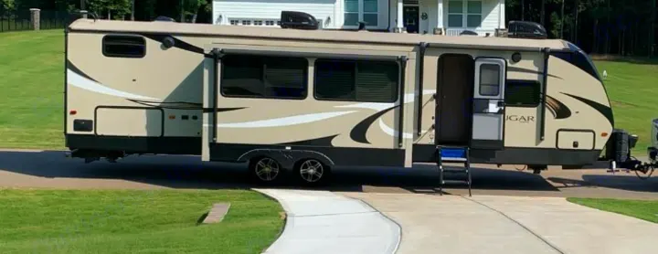 Spacious beige and black travel trailer RV with steps and awning extended, parked on a paved driveway. Ideal for an rv rental.. Keystone RV Cougar 2019