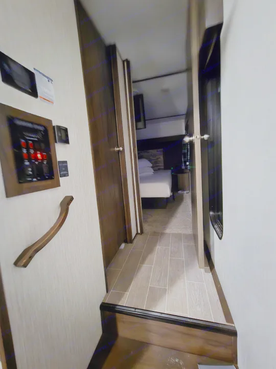 RV rental interior: narrow hallway leads to a bedroom with a white bed; a control panel is on the left wall.. Forest River Cherokee Arctic Wolf 2019