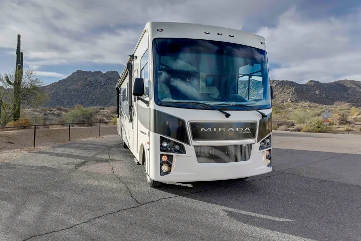 A white & black Mirada RV rental parked in a desert landscape. Mountains & a saguaro cactus are visible under a cloudy sky.. Coachmen Mirada 35OS 2023