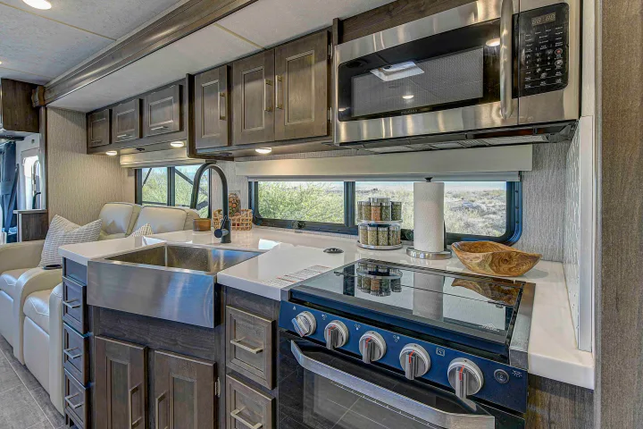 Modern RV rental kitchen and living area, featuring a large sink, stove, microwave, and scenic window view.. Coachmen Mirada 35OS 2023