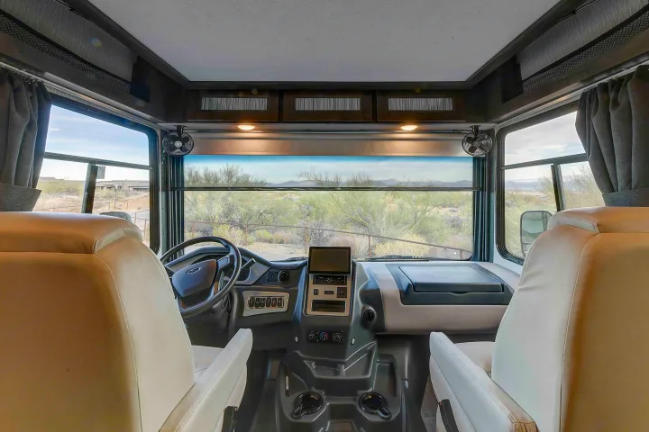 Spacious RV rental cockpit with light-colored seats, detailed dashboard, and a wide windshield view of a desert landscape.. Coachmen Mirada 35OS 2023