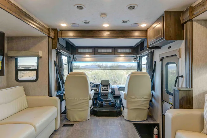 Bright RV rental interior showing the cockpit, driver & passenger seats, and a beige sofa living space.. Coachmen Mirada 35OS 2023