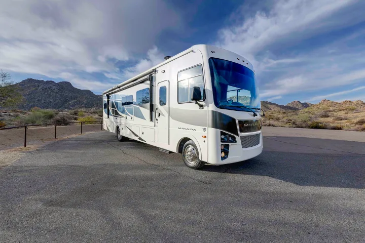 White Mirada RV rental parked on asphalt, set against desert mountains under a partly cloudy sky.. Coachmen Mirada 35OS 2023
