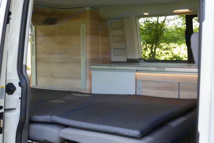 RV rental van interior: a cozy folded bed, built-in fridge, wood-grain cabinets, and a window view. Ready for adventure!. Volkswagen California Coast T6 2020