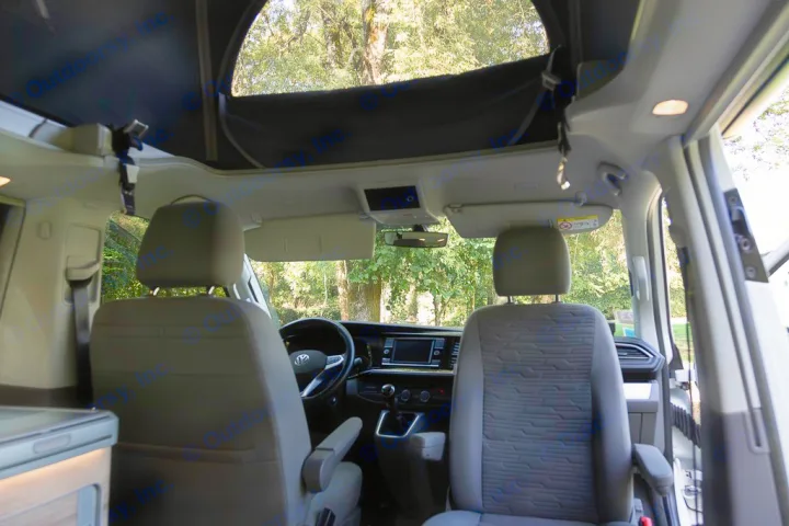 Interior view of an RV rental campervan, showing front cabin, dashboard, and open pop-top roof with trees visible.. Volkswagen California Coast T6 2020