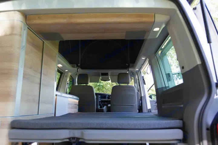 RV rental interior showing a comfortable bed, wood cabinets, and a pop-top roof, perfect for camping travel adventures.. Volkswagen California Coast T6 2020