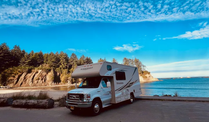 Winnebago RV rental parked by a beautiful beach and forested coast.. Winnebago Minnie Winnie 2017