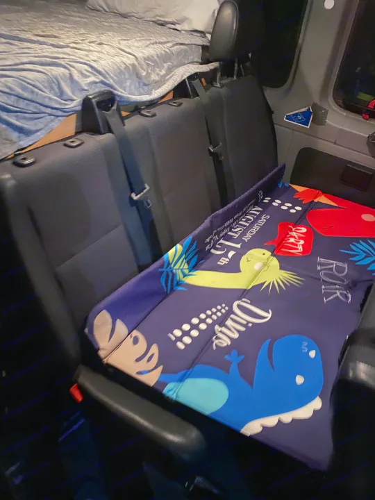 RV rental camper van interior featuring a cozy bed, passenger seats, and a fun dinosaur mat for kids.. Mercedes Sprinter 2011