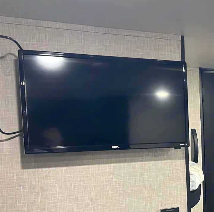 A black Onn Roku TV mounted on a textured wall in an RV rental, with a power cord visible on the left.. Jayco Jay Flight SLX 260BH 2025