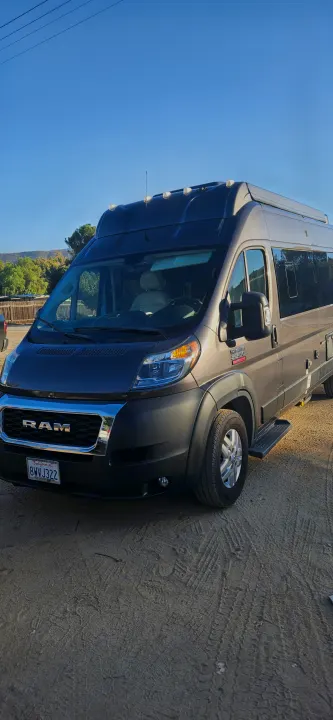 Gray high-roof Ram ProMaster camper van, parked on dirt. Perfect for your next RV rental.. Thor Tellaro 2022