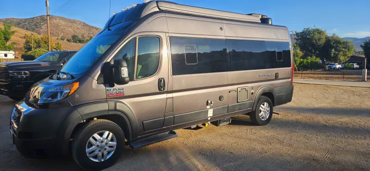 Your next RV rental adventure! This grey Ram ProMaster camper van is parked on a sunny gravel lot, ready for the open road.. Thor Tellaro 2022