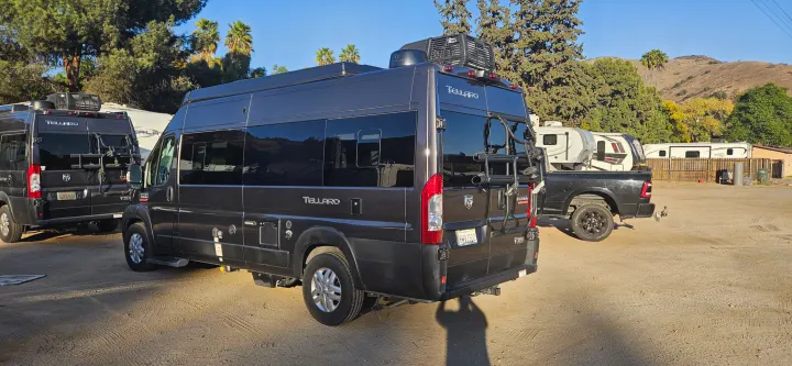 Two Ram ProMaster Tellaro camper vans, possibly rv rental units, are parked in a sunny RV park.. Thor Tellaro 2022