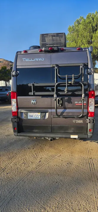 Thor Tellaro RV rental, a gray camper van with a rear bike rack, parked on dirt. Ideal for outdoor adventures.. Thor Tellaro 2022