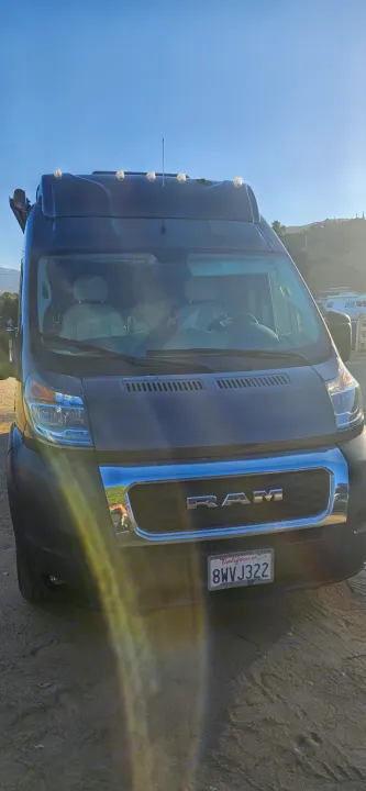 Front of a dark grey Ram ProMaster camper van, an RV rental, parked on dirt. CA license 8WVJ322 visible.. Thor Tellaro 2022