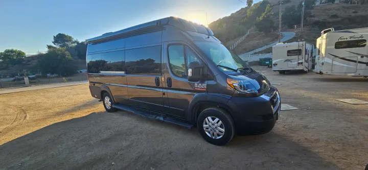 Dark grey Telluro Ram ProMaster 3500 campervan RV rental parked on dirt, with other RVs and a hillside in background.. Thor Tellaro 2022