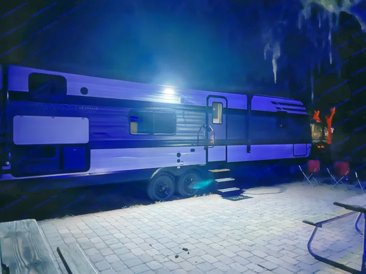 Experience an RV rental under the stars! This illuminated travel trailer shines bright at a cozy night campsite.. Grand Design Transcend Xplor 2024