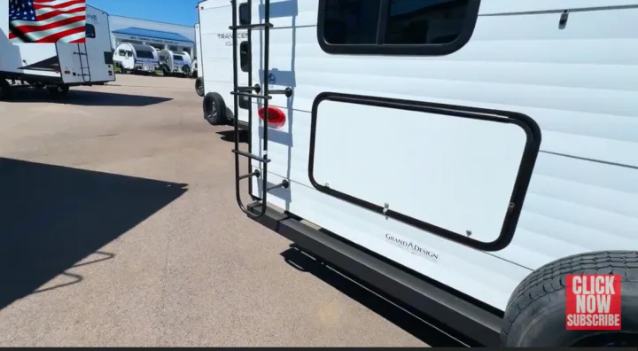 Rear view of a white Grand Design RV rental travel trailer, showing a ladder, storage compartment, and spare tire at an outdoor lot.. Grand Design Transcend Xplor 2024