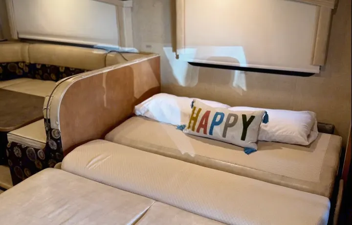 RV rental interior: Dinette seating on the left, and a bed with a 'HAPPY' pillow on the right.. Winnebago Minnie Winnie Premier 2015