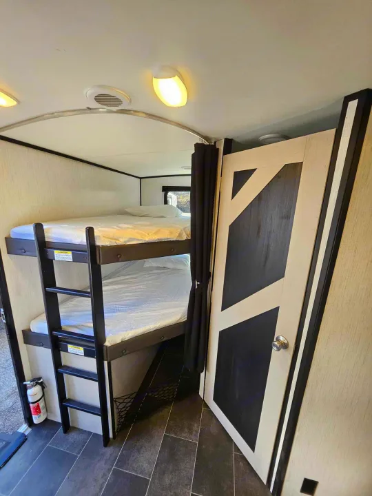 Modern RV rental interior showing two-tier bunk beds with a ladder, stylish patterned door, and safety extinguisher.. Heartland mallard 2022