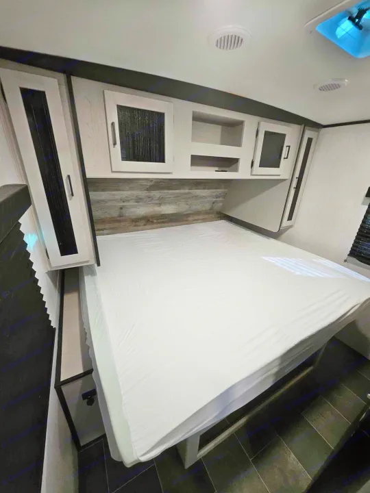 Cozy RV rental bedroom featuring a queen bed, overhead storage cabinets, and a modern wood-paneled headboard.. Heartland mallard 2022