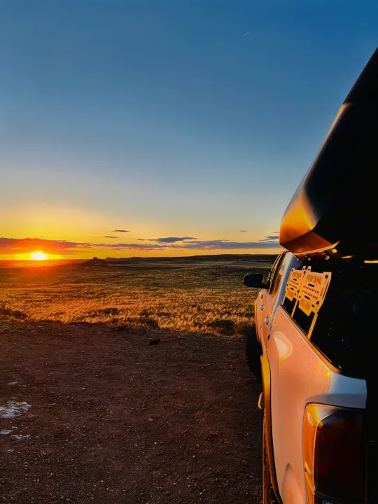 White pickup truck with rooftop camper faces a golden sunset over fields. Ideal RV rental scene for nature exploration.. Toyota Tacoma TRD-Pro 2020