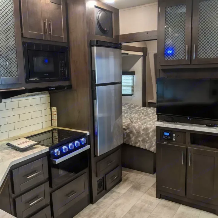 Modern RV rental interior featuring a full kitchen with microwave, stove, and fridge, plus a cozy bedroom area.. Grand Design Momentum Toy Hauler 2022