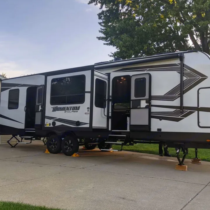 This white Momentum G-Class RV is set up with slide-outs extended, ready for an RV rental adventure.. Grand Design Momentum Toy Hauler 2022