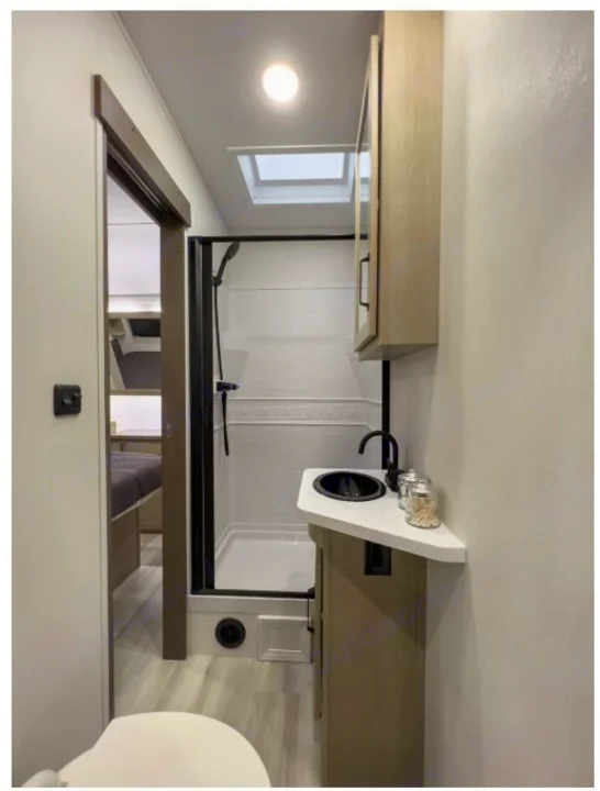 Modern RV rental bathroom with a full shower, compact vanity, sink, and toilet. Bedroom visible through the doorway.. Grand Design Momentum Toy Hauler 2022