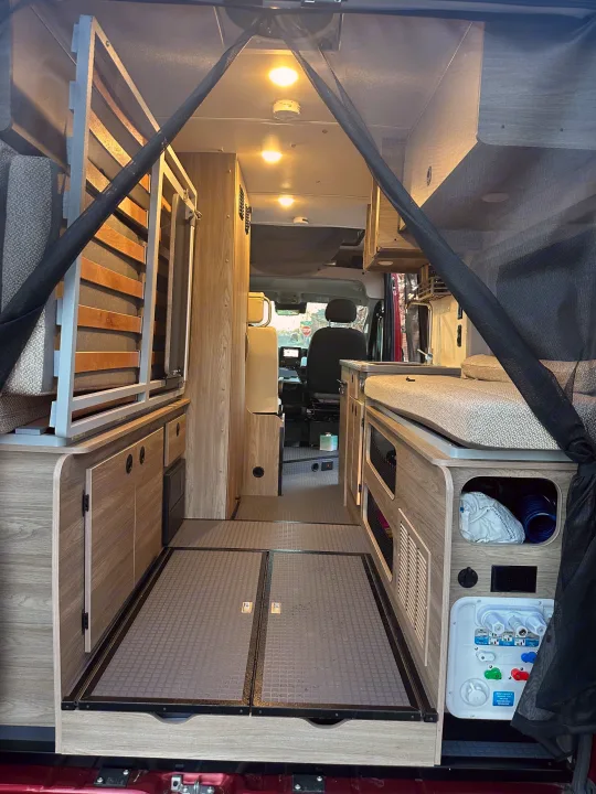RV rental interior: A spacious van conversion with a convertible bed, storage, and water utility panel leading to the cockpit.. Winnebago Solis 2023