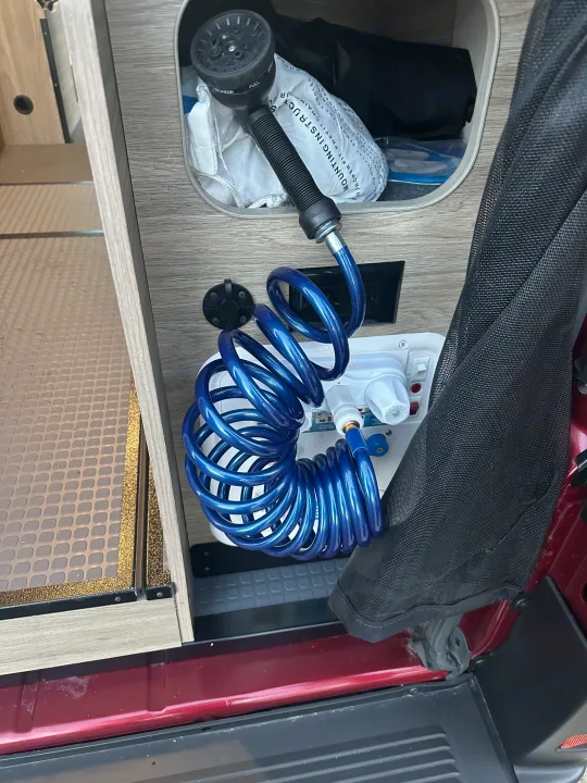 RV rental utility setup: a blue coiled outdoor shower hose with an adjustable head, ready for use. Perfect for camp life.. Winnebago Solis 2023