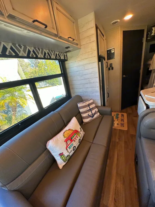 Inside a modern rv rental: grey sofa with fun pillows, rustic wall, and bright windows offering scenic views.. Entegra Coach 29F 2021