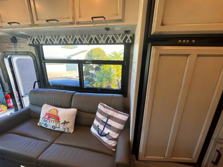 Cozy rv rental interior featuring a comfy sofa with decorative pillows, large window views, and accessible cabinets.. Entegra Coach 29F 2021