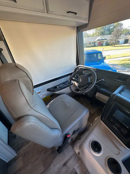 RV rental driver's cockpit interior, showcasing a tan seat, Ford steering wheel, and pull-down windshield shade.. Entegra Coach 29F 2021