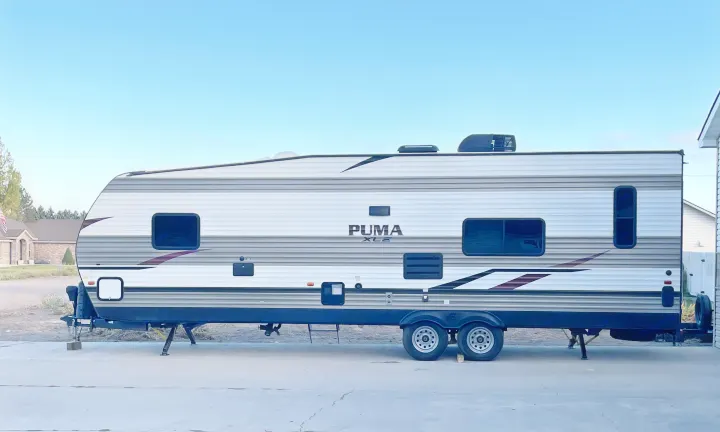 Side view of a modern Puma XLE travel trailer, perfect for an RV rental, parked on concrete.. Palomino Puma 2021