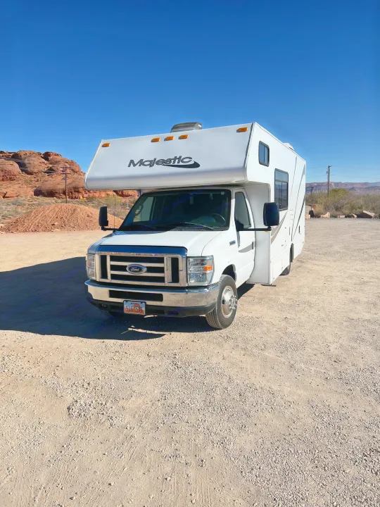 White Majestic RV rental parked in a sunny Utah desert with red rock mountains under a clear blue sky.. Thor Majestic 2018
