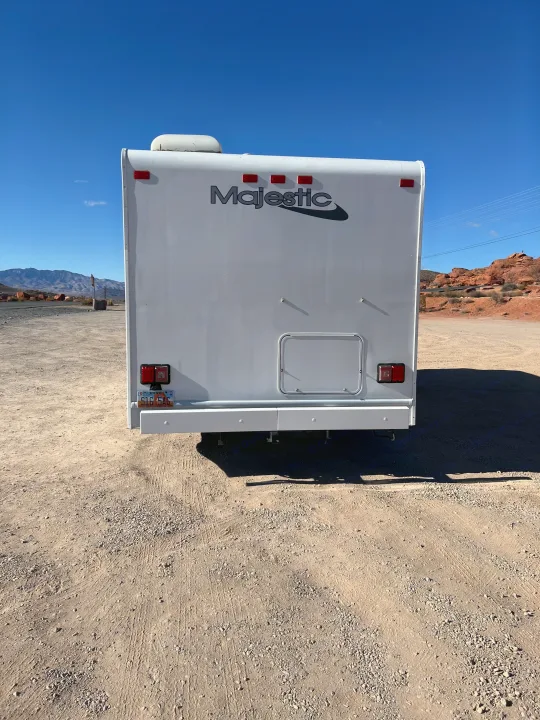 Majestic RV rental from behind, parked on dirt with mountains & red rocks under a blue sky. Utah license plate visible.. Thor Majestic 2018