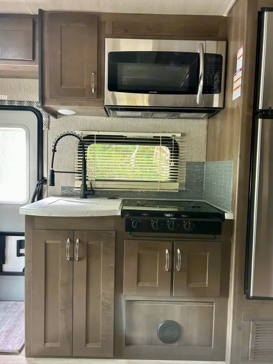 This RV rental features a modern kitchen with a stainless steel microwave, black stove, sink, and wood-look cabinets.. Nexus RV Phantom 2023