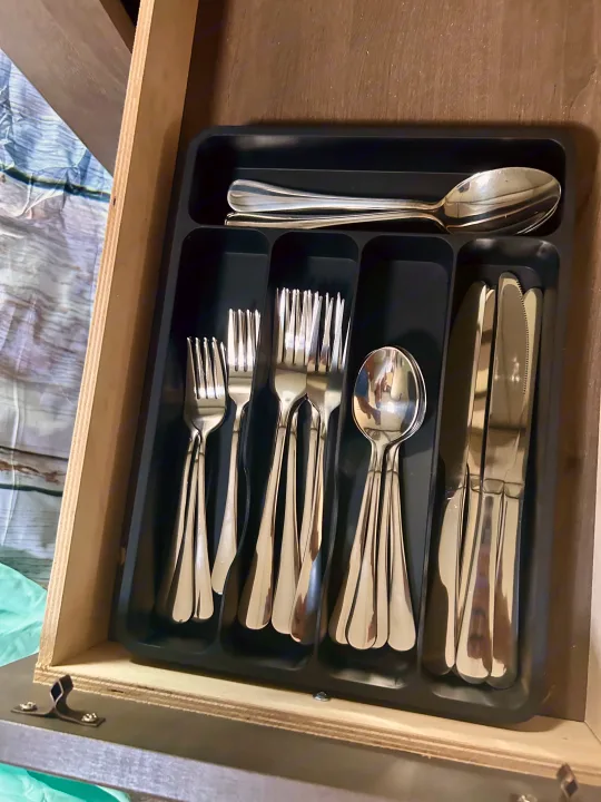 A drawer with a black cutlery organizer filled with shiny forks, spoons, and knives, ideal for an RV rental.. Nexus RV Phantom 2023