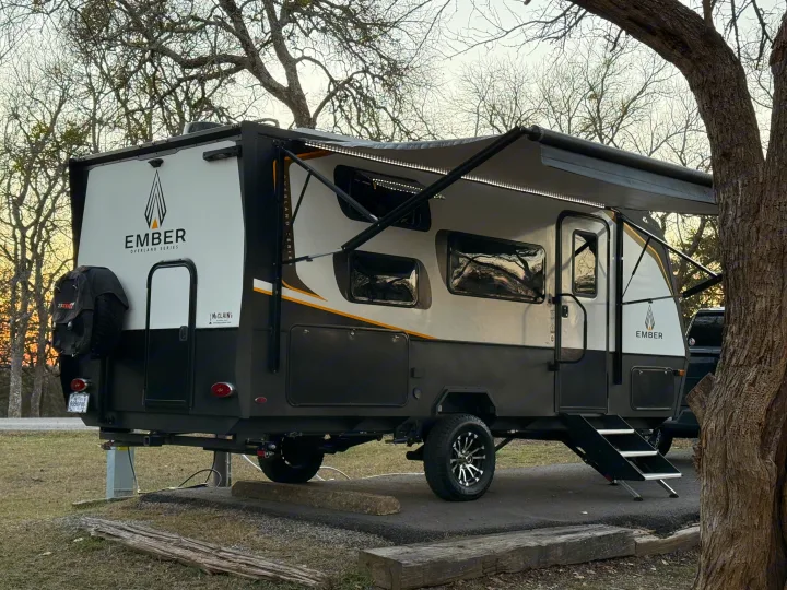 Ember Overland Series RV rental parked at a serene campsite with awning extended and trees overhead for peaceful camping.. Ember Overland 2023