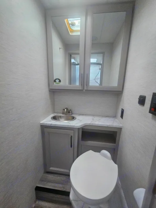 Efficient RV rental bathroom: toilet, vanity with sink, and medicine cabinet. Skylight visible in mirror reflection.. Thor Coleman 28AMC 2024