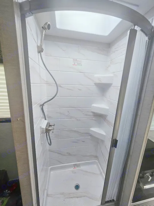 Explore this clean & compact shower in an RV rental, featuring a handheld showerhead, corner shelves, and a skylight.. Thor Coleman 28AMC 2024