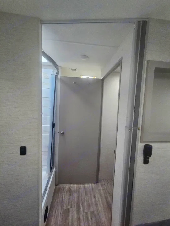Inside an rv rental: A modern RV interior features a compact shower, central door, and hallway leading to other areas.. Thor Coleman 28AMC 2024